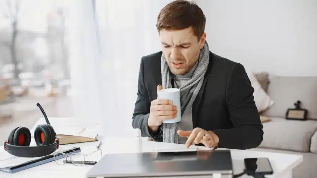 Zzp'er die zich ziek voelt en met thee achter zijn laptop thuis werkt