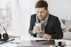 Zzp'er die zich ziek voelt en met thee achter zijn laptop thuis werkt