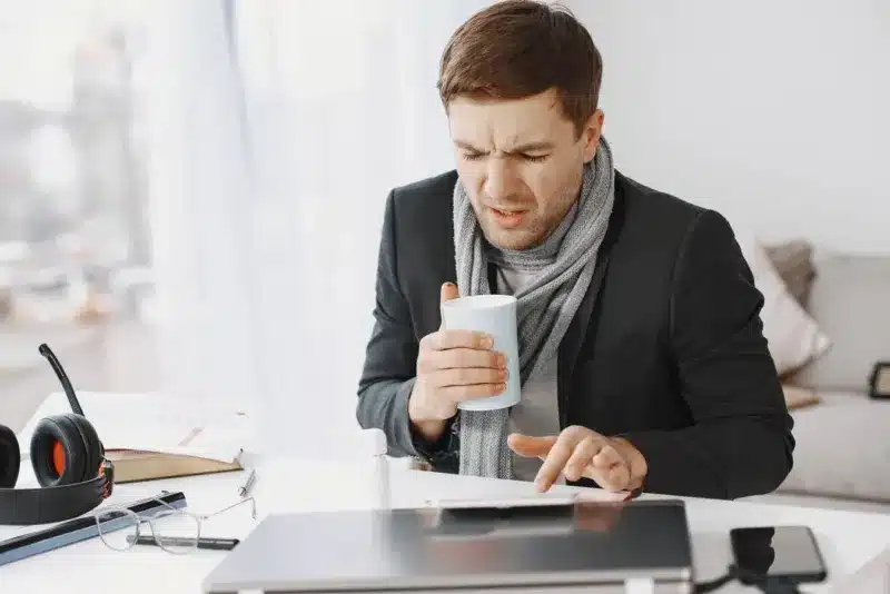 Zzp'er die zich ziek voelt en met thee achter zijn laptop thuis werkt