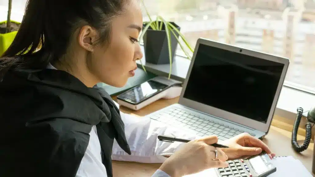 Zzp'er werkt aan haar administratie met laptop en rekenmachine in een licht kantoor
