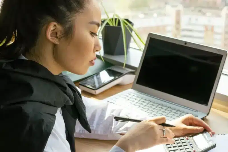 Zzp'er werkt aan haar administratie met laptop en rekenmachine in een licht kantoor
