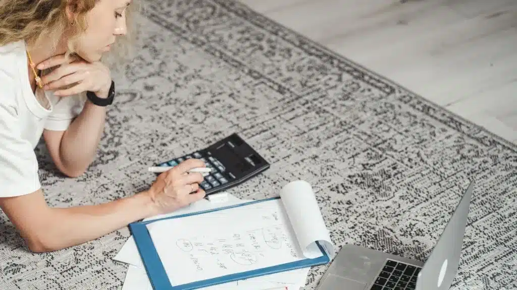 Vrouw berekent thuis met rekenmachine en laptop haar netto inkomen als zzp'er