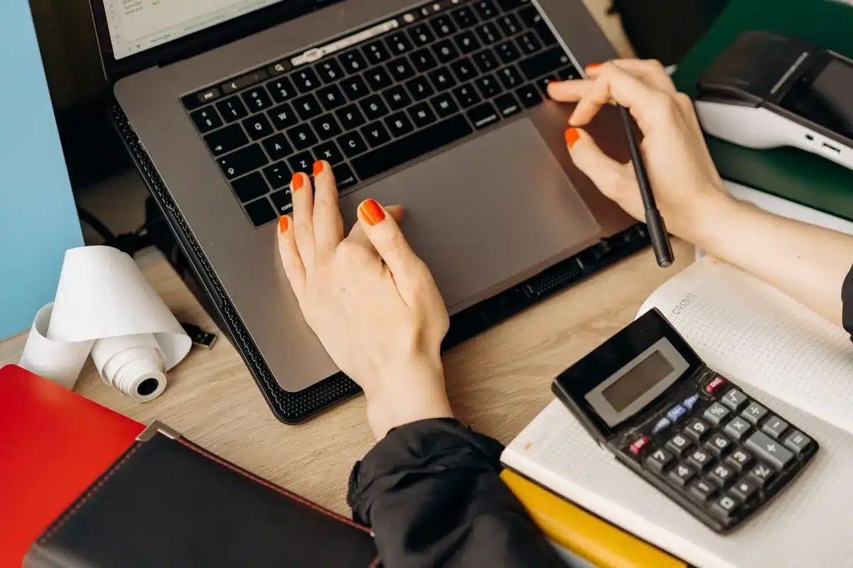 Freelancer berekent met rekenmachine en laptop de btw voor een nieuwe factuur