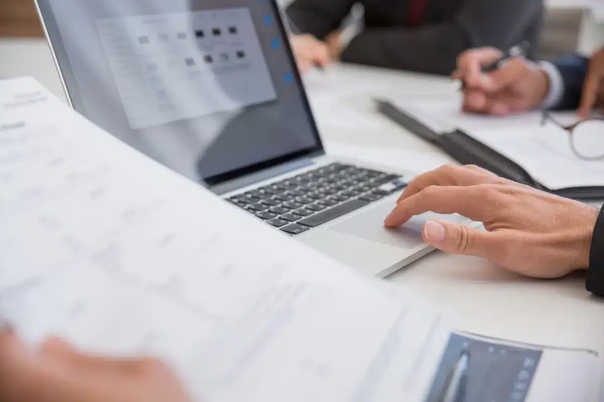 Handen werken aan documenten en laptop bij het opstellen van een offerte voorbeeld
