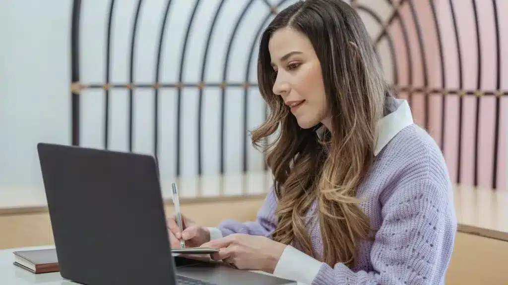 Zzp'er maakt aantekeningen naast haar laptop terwijl ze een factuur opstelt