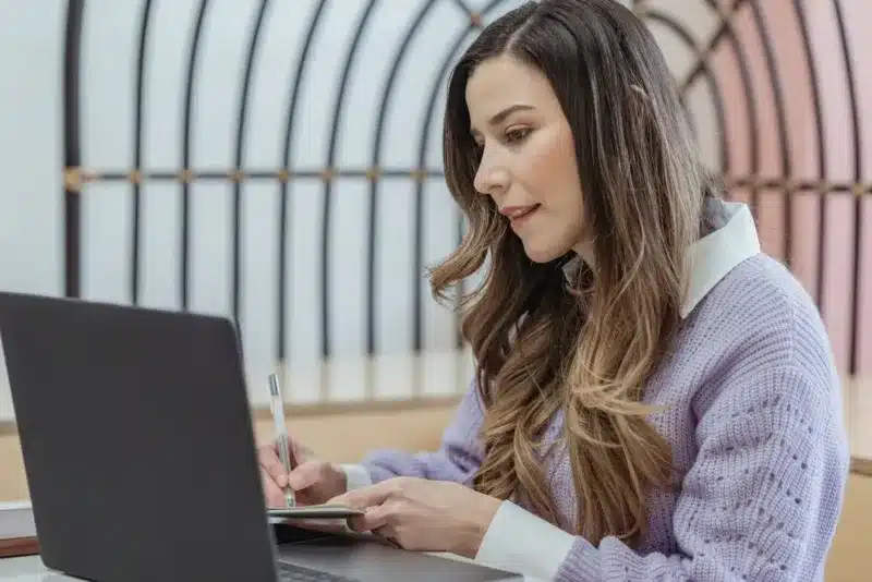 Zzp'er maakt aantekeningen naast haar laptop terwijl ze een factuur opstelt